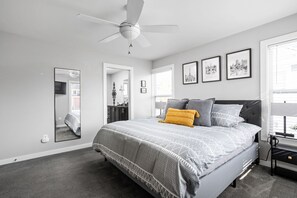 Une chambre à coucher avec un lit, un ventilateur de plafond, un grand miroir et des tableaux encadrés accrochés au mur.