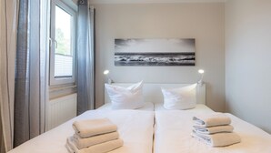 Ein ordentlich bezogenes Bett mit weißen Leinen und Handtüchern, ein Fenster mit Vorhängen und ein Bild an der Wand.