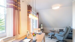 Ein modernes Wohnzimmer mit Essbereich, ausgestattet mit einem Holztisch, einem grauen Sessel und einer Couch.