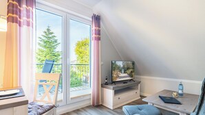 Ein Zimmer mit Balkon, Fernseher, Schreibtisch und Stuhl.