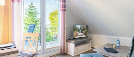 A room with a balcony, a TV, a desk, and a chair.