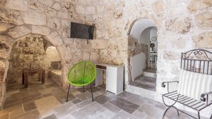 A stone-walled room with a green chair, a white cabinet, and a metal bench. - 4197 Villa Irma by Barbarhouse (Carovigno)