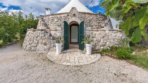 A stone building with a conical roof, a central entrance with green shutters, and potted plants on either side. - 4197 Villa Irma by Barbarhouse (Carovigno)