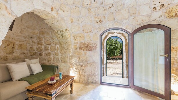 A stone-walled room with a wooden table, a sofa, and a door leading outside. - 4197 Villa Irma by Barbarhouse (Carovigno)