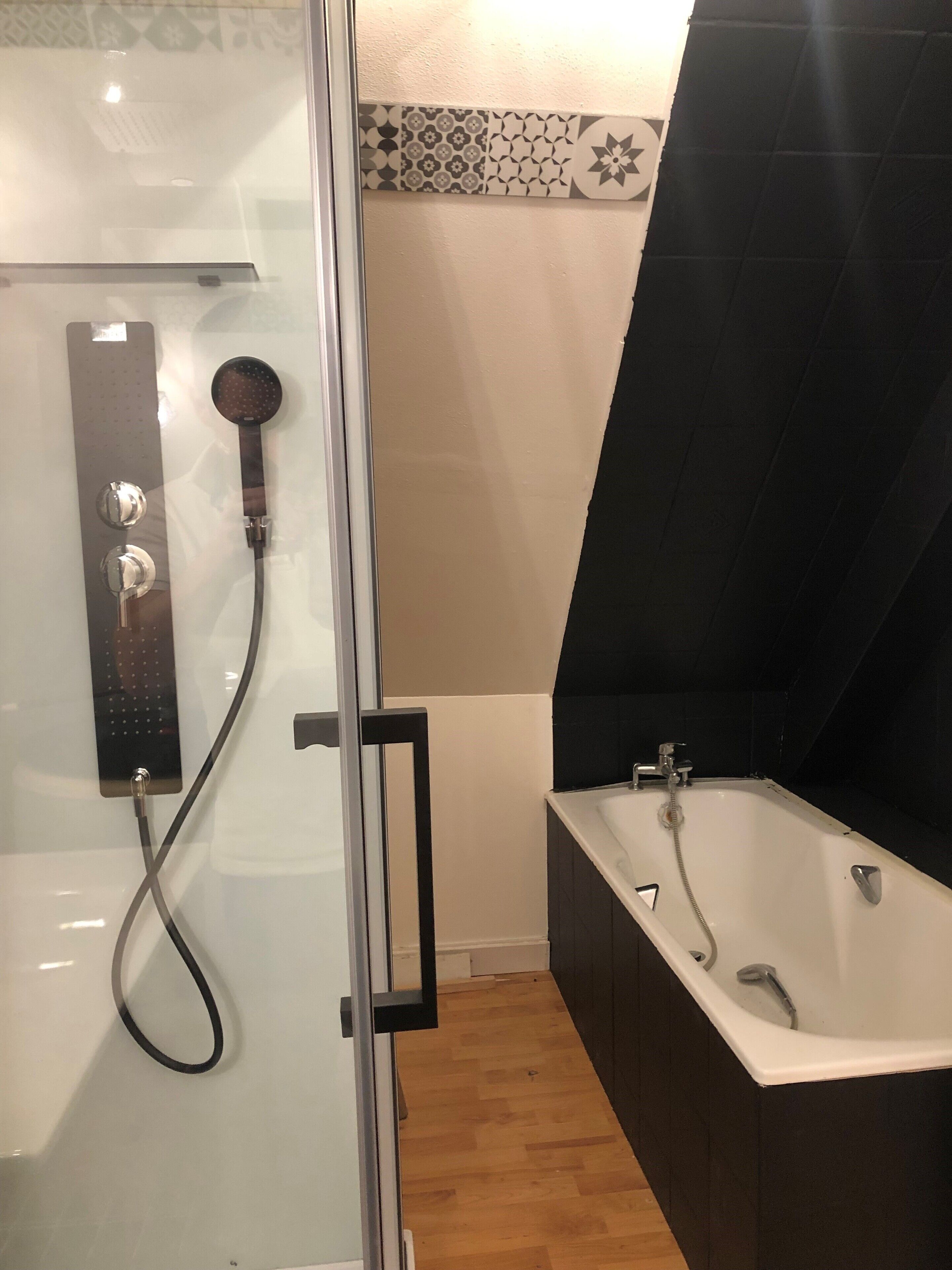 Une salle de bain moderne dotée d’une douche à parois de verre, d’une baignoire sur pieds et d’un mur recouvert de carreaux.