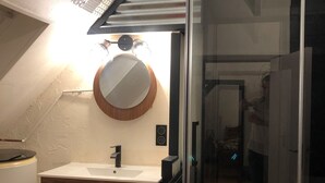 Een badkamer met een houten wastafelmeubel, een ronde spiegel en een douchecabine van glas.