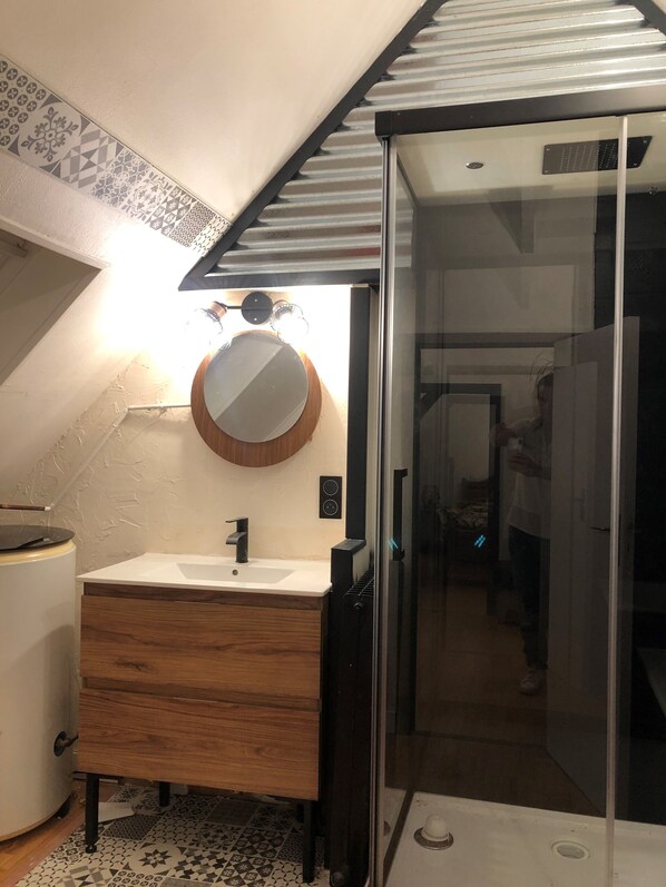 A bathroom with a wooden vanity, a round mirror, and a glass shower enclosure.