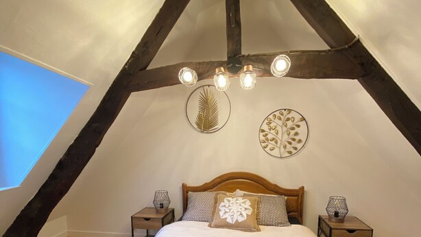 Een slaapkamer met een schuine kap, een houten bed, twee nachtkastjes en decoratieve wandkunst.