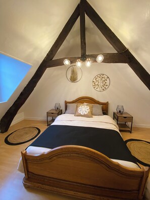 A bedroom with a sloped ceiling, a wooden bed, two bedside tables, and decorative wall art.