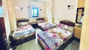 Habitación de hotel con dos camas individuales, una ventana pequeña, un ventilador de techo y un espejo en la pared.