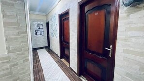 Un pasillo con dos puertas de madera, cada una con un número. Las paredes tienen un diseño que imita la piedra, y el suelo está cubierto de baldosas.