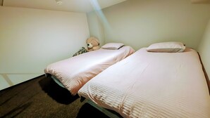 Une chambre avec deux lits, un ours en peluche et un mur uni.