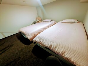 Una habitación con dos camas, un osito de peluche y una pared lisa.