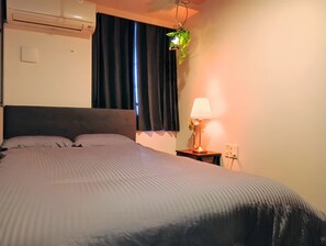 Een bed met hoofdbord, een bedlampje en een raam met gordijnen.
