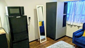 Un espace de vie compact comprenant un réfrigérateur noir, un four à micro-ondes placé au-dessus, un canapé bleu et un grand miroir.