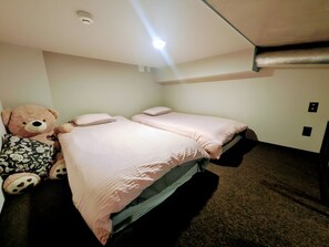Une chambre avec deux lits, un grand ours en peluche et un luminaire au plafond.
