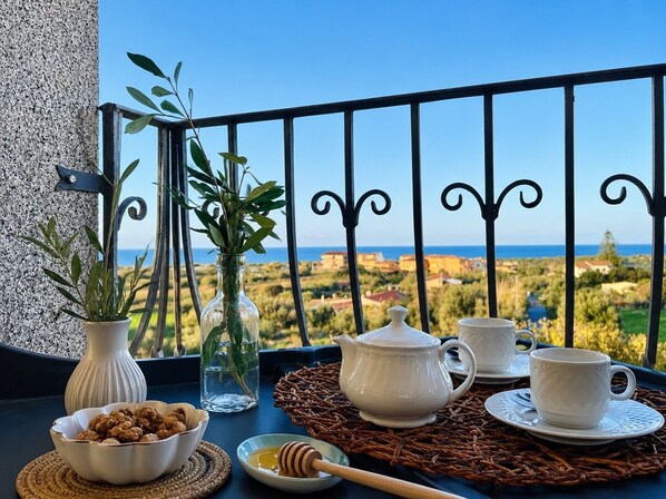 Ein Balkon mit Blick auf das Meer, ein Tisch mit Teekanne, Tassen, einer Nuss-Schale und einem Honiglöffel.