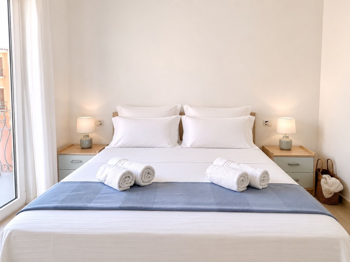 A hotel room with a bed, two bedside tables with lamps, a window with curtains, and a view of the outside.