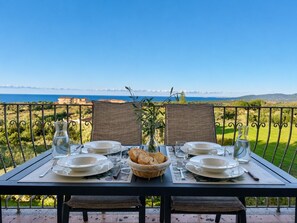 A table set for four with plates, glasses, and a basket of bread, overlooking a scenic landscape. - Chris House Key to Villas (Sardegna)