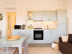 A compact kitchen with a microwave, coffee maker, and gas stove. There is a dining table with chairs and a glass-top table.