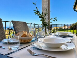 A dining table set outdoors with a clear view of the sea, a vase with greenery, and a basket of bread. - Chris House Key to Villas (Sardegna)