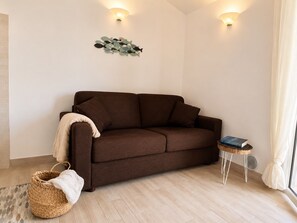 A brown sofa, a woven basket, a small table with a book, and a wall-mounted light fixture.