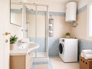 A bathroom with a shower, sink, and washing machine. - Chris House Key to Villas (Sardegna)