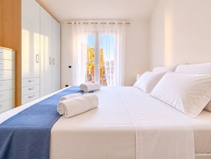A hotel room with a bed, a wardrobe, and a view of buildings through the window.