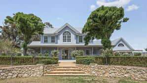 A large, two-story house with a stone pathway leading to the front door, surrounded by well-maintained hedges and trees. - Chateau On Vines ~ Aldinga - Welcome to Chateau On Vines (Aldinga)
