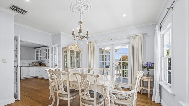 A dining area with a chandelier, white furniture, and a view of the outside. - Chateau On Vines ~ Aldinga - Welcome to Chateau On Vines (Aldinga)