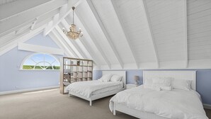 Quarto com duas camas, uma janela grande e teto inclinado.