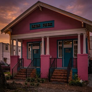 A two-story house with a pink facade, white trim, and blue accents on the doors and windows.