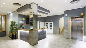 A modern reception area with a counter, a staircase, and an elevator. - VTZ Hotel El Príncipe (Zaragoza)