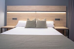 Quarto de hotel moderno com uma cama grande, duas mesas de cabeceira e uma cabeceira de madeira com iluminação embutida.