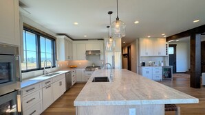 Una cocina moderna con una isla grande, muebles blancos, electrodomésticos de acero inoxidable e iluminación colgante.