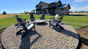 Una casa moderna con fachada de piedra y un patio con cuatro sillas Adirondack y una mesa redonda.