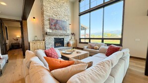 Una sala de estar con chimenea de piedra, ventanas amplias y vistas al exterior.