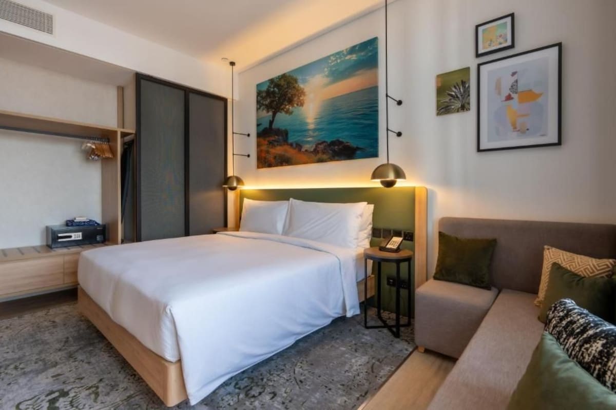 Ein Hotelzimmer mit Bett, Schlafsofa, Nachttisch und einem Gemälde von einem Baum am Meer.