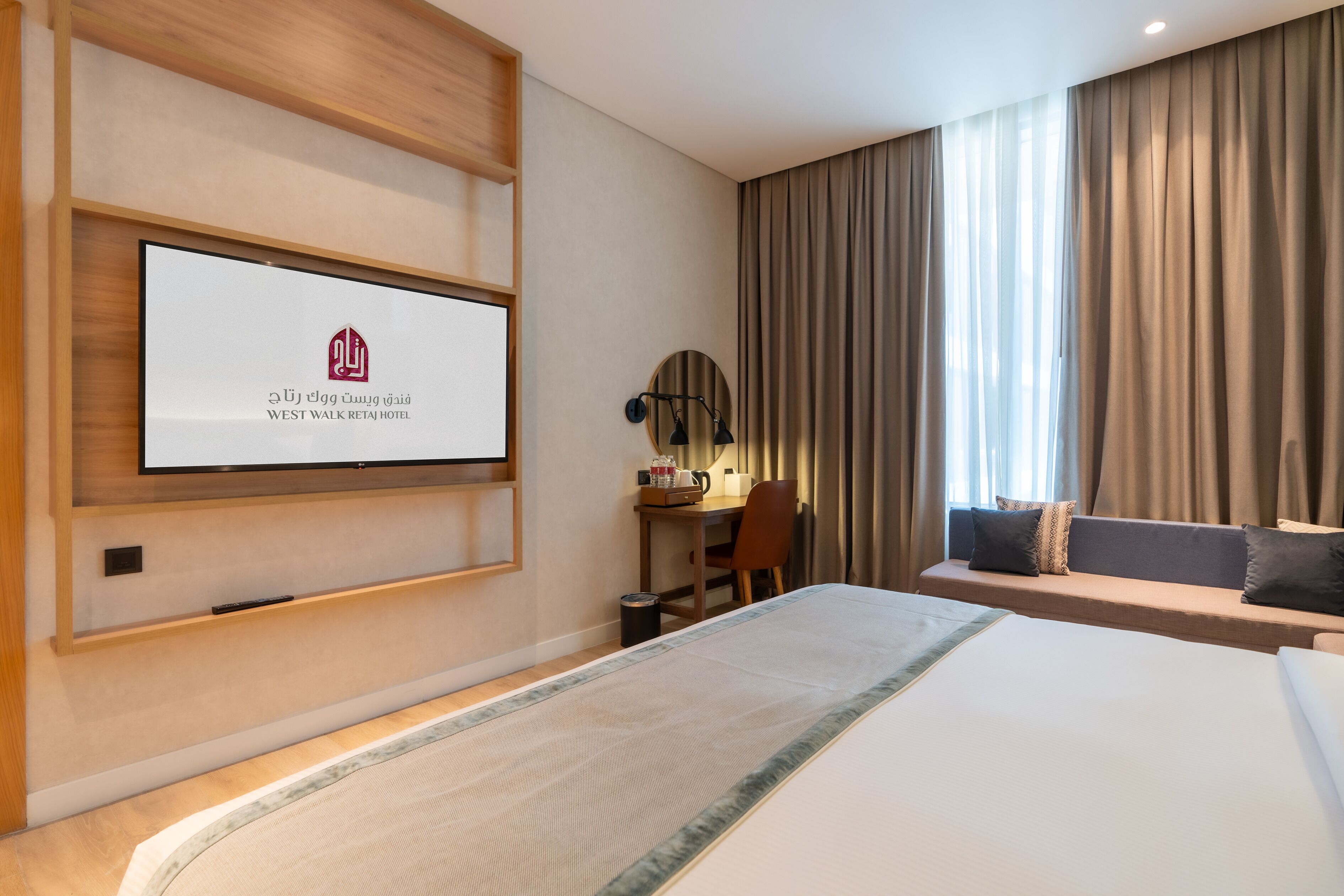 Una habitación de hotel con cama, escritorio, silla y un ventanal con cortinas.