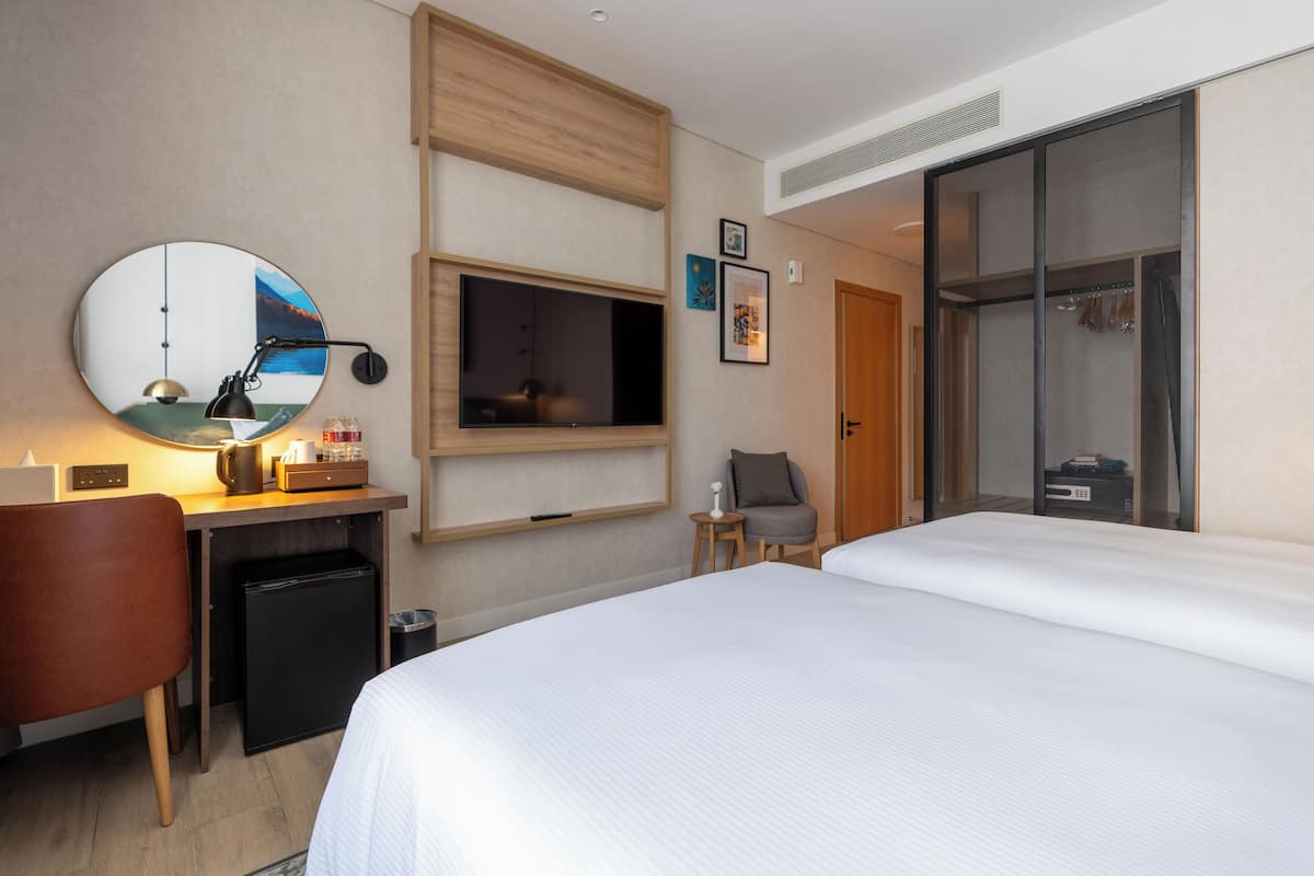 A hotel room with a bed, a desk with a computer, a TV, and a small chair.