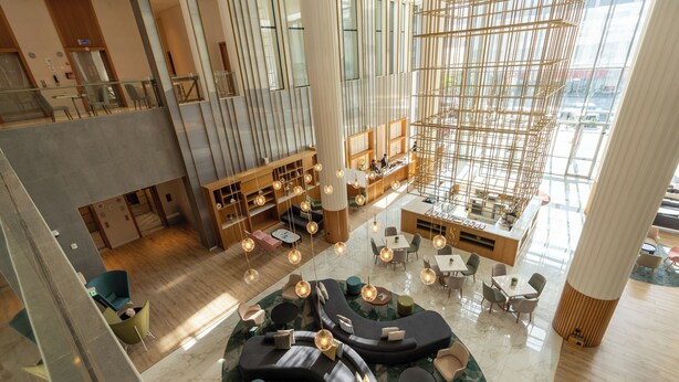 Eine geräumige Lobby mit hoher Decke, modernen Sitzbereichen und einem großen, offenen Raum mit Holzkonstruktion.