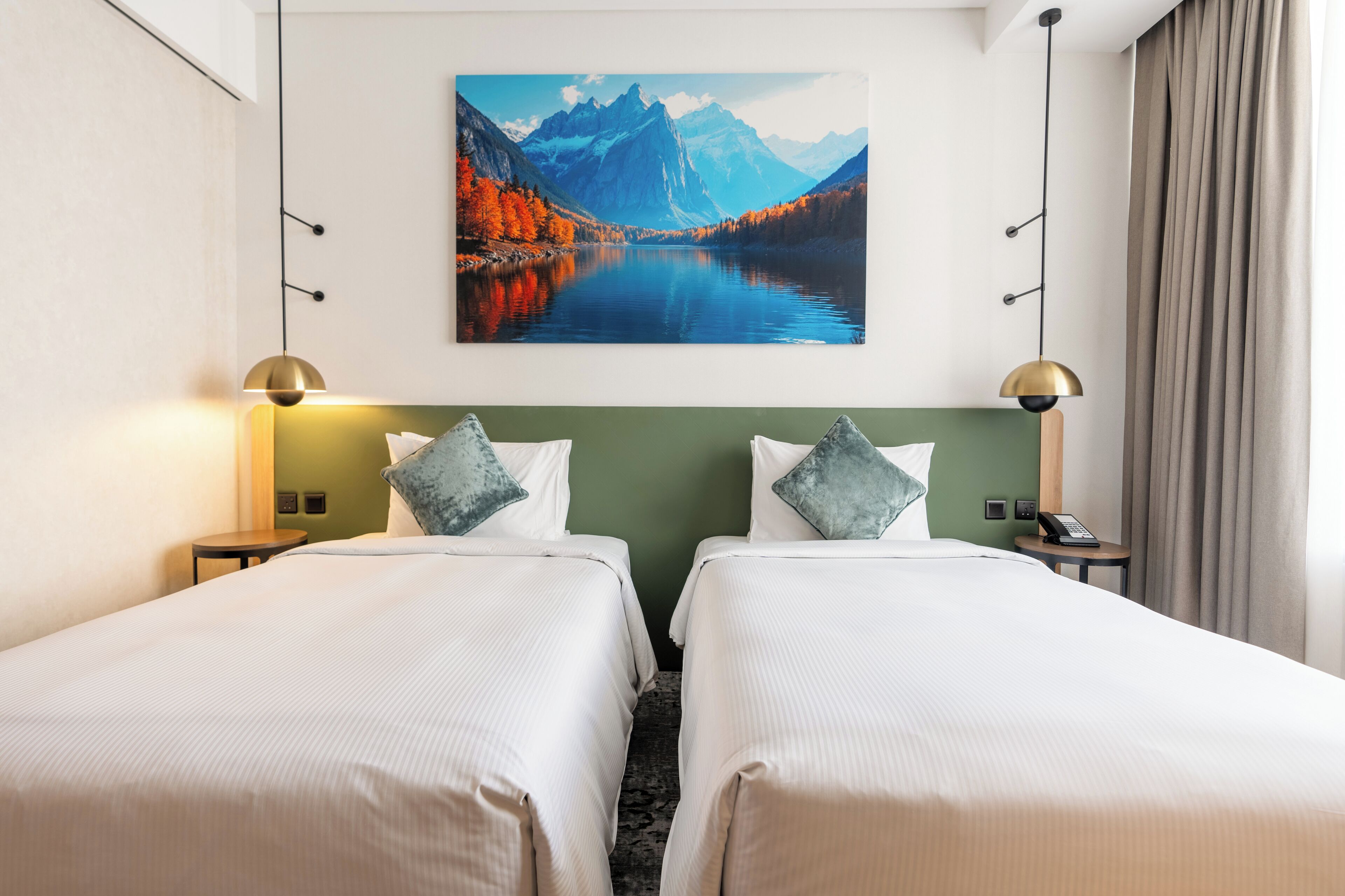 Una habitación de hotel con dos camas, un cuadro de un lago de montaña y un teléfono en una mesita de noche.