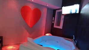 A modern bedroom with a large red heart on the wall, a TV mounted on the wall, and a bathtub labeled 'LIVING B&B'. - Living (Casoria)