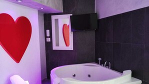 A modern bathroom with a large bathtub labeled 'LIVING B&B', a red heart decoration, and a white towel stand. - Living (Casoria)