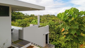 Una casa moderna con techo plano, balcón y vista a exuberante vegetación.