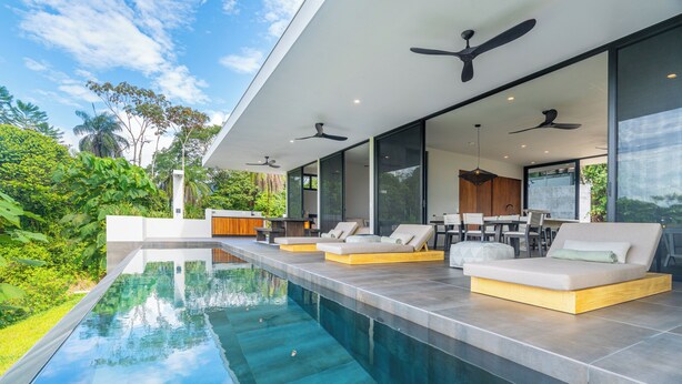 Un área de piscina exterior moderna con asientos incorporados y ventiladores de techo.