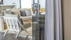 Una sala de estar moderna con un sofá blanco, una silla de madera y un separador de vidrio.