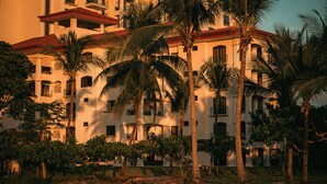 Ein mehrstöckiges Hotel mit Balkonen, Palmen und einem roten Dach.