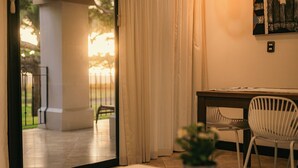 Ein Zimmer mit einem Tisch, zwei Stühlen, einer Topfpflanze und Blick durch eine Glastür auf einen Außenbereich mit Geländer.