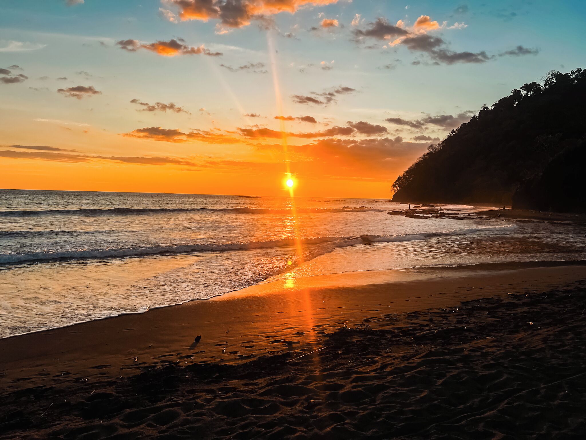 A beach at sunset with the sun low on the horizon, casting a golden glow over the water and sand.